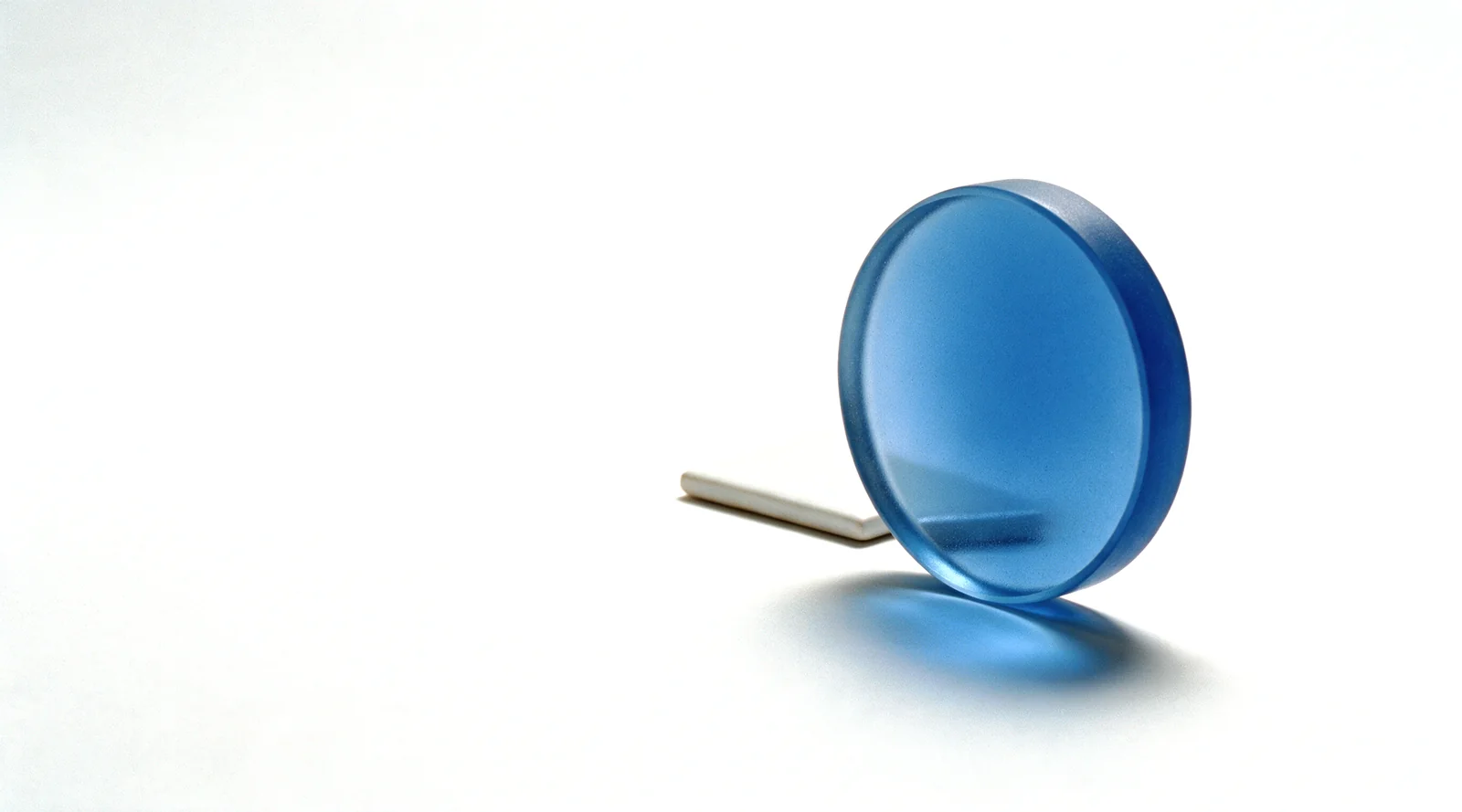 A thick frosted blue glass lens standing over a white ceramic tile on a white studio ground