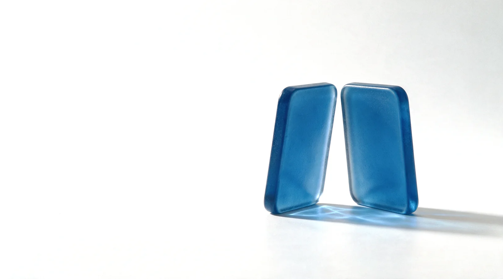 Two frosted blue glass tiles standing face to face on a white studio ground