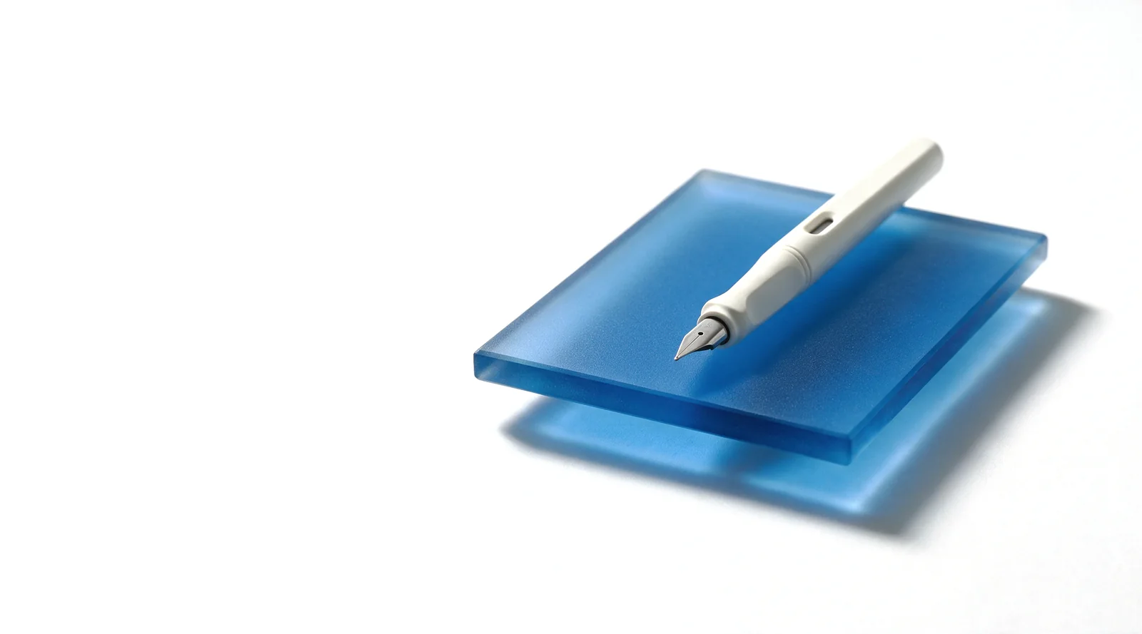 A white ceramic pen resting across a frosted blue glass slab on a white studio ground